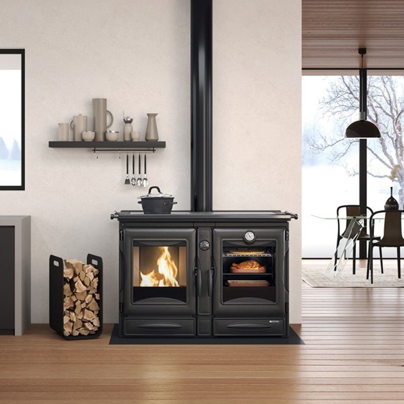 Cuisinière à bois Alaska 12kW noire en fonte avec poêle et four dans une cuisine moderne avec étagère et bûches.